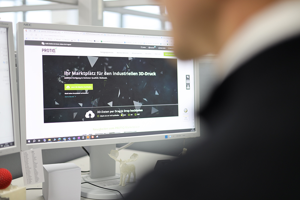 Ein Mensch sitzt vor einem PC-Bildschirm, auf dem protiq.com geöffnet ist.